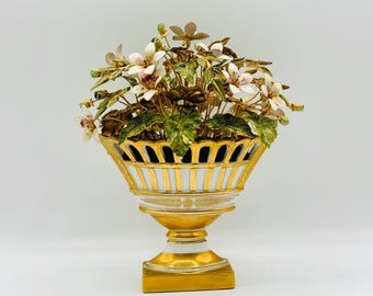 May include: A white porcelain vase with gold accents and a delicate floral design. The vase is decorated with a bouquet of white and green flowers.