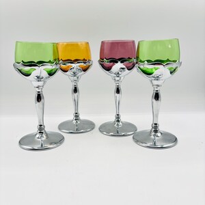 Puede incluir: Cuatro copas con cuencos de cristal de colores y bases de metal plateado. Los cuencos son de color verde lima, ámbar, magenta y verde lima. Cada copa presenta un revestimiento decorativo de metal plateado con un borde festoneado.