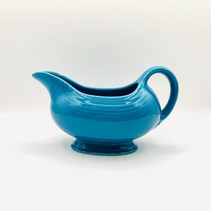 May include: A turquoise blue ceramic gravy boat with a wide, rounded base and a single handle.