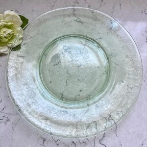 May include: A vintage green glass dinner plate with a delicate floral pattern around the rim.