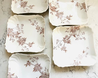 May include: Set of five square ceramic plates with a white background and a brown floral pattern. The plates have a scalloped edge.