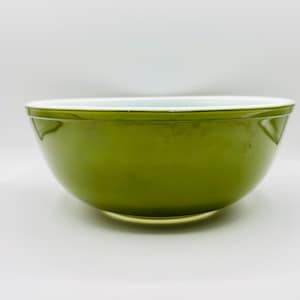 May include: A round mixing bowl with a smooth, glossy olive green exterior and a contrasting white interior. The bowl features a simple, wide rim and a curved base, presenting a clean, functional design for kitchen use and food preparation.