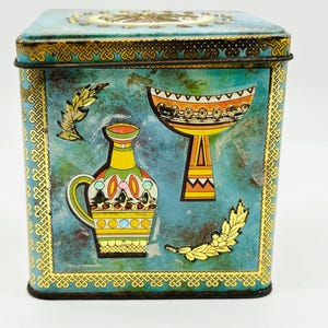 May include: Square teal blue tin box with a gold trim and a design of two stylized vases with geometric patterns. The vases are in shades of yellow, orange, red, and green.