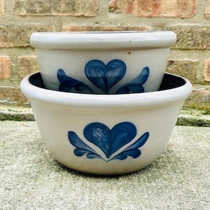 Può includere: Due ciotole in ceramica blu e bianca con un design a forma di cuore. Le ciotole sono impilate l'una sull'altra.