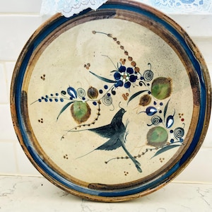 Puede incluir: Un plato de cerámica con un diseño floral azul, verde y marrón y un pájaro negro. El plato tiene un borde marrón con una banda azul.