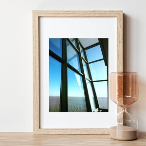 Puede incluir: Una fotografía enmarcada de una vista a través de una gran ventana con múltiples paneles. La ventana está en ángulo y la vista muestra un cielo azul y una masa de agua. El marco está hecho de madera clara.