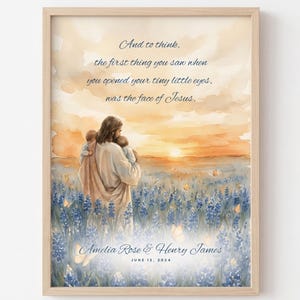 May include: A framed watercolor print featuring a figure in robes holding two infants in a field of blue flowers at sunset. The text reads: And to think, the first thing you saw when you opened your tiny little eyes, was the face of Jesus. Amelia Rose & Henry James, June 12, 2024.