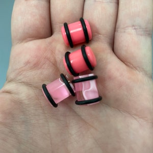 May include: Four pink acrylic ear gauges with black o-rings. Two gauges are solid pink and two have a white swirl pattern.