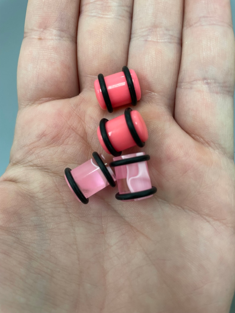 May include: Four pink acrylic ear gauges with black o-rings. Two gauges are solid pink and two have a white swirl pattern.