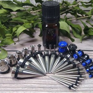 May include: A set of 16 stainless steel ear gauges, including a variety of sizes and styles. The set includes a small bottle of oil, likely for cleaning and lubrication. The gauges are a mix of plain and patterned, with some featuring a blue and white speckled design.