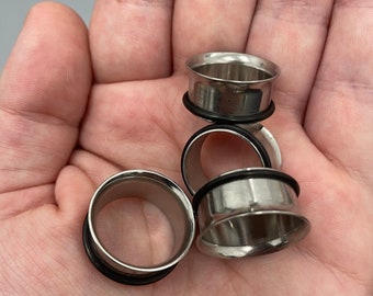 May include: Four silver ear gauges with black rubber o-rings. The gauges are stacked on top of each other.