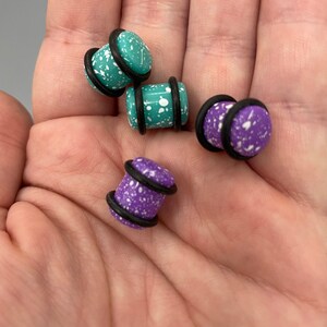 May include: Four pairs of ear gauges with black o-rings. Two pairs are teal with white speckles and two pairs are purple with white speckles.
