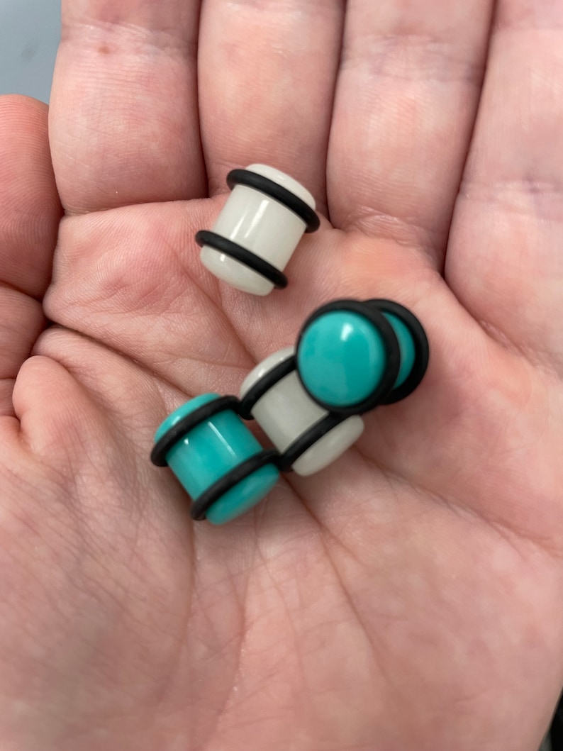 May include: A set of four ear gauges, two are white with black trim and two are turquoise with black trim.
