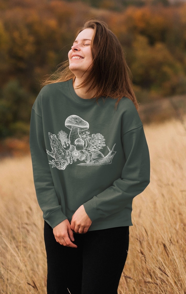 May include: A dark green sweatshirt with a white graphic print of a mushroom, snail, and frog. The graphic is a vintage style illustration.