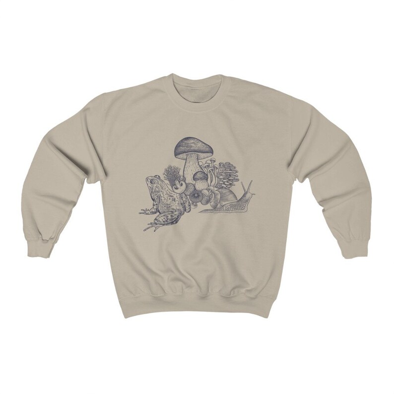 May include: A beige sweatshirt with a blue illustration of a frog, snail, and mushrooms. The illustration is centered on the sweatshirt.