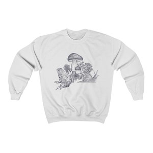 May include: A white sweatshirt with a blue and white illustration of a frog, snail, and mushrooms. The illustration is centered on the sweatshirt.