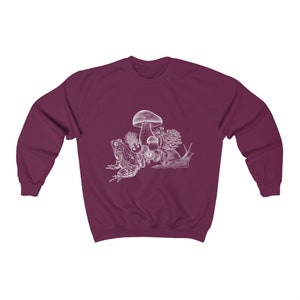 May include: A maroon sweatshirt with a white graphic of a frog, snail, and mushrooms.