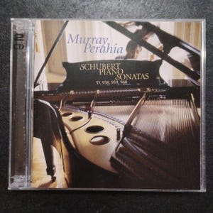 May include: A CD case featuring Murray Perahia's album, "Schubert Piano Sonatas." The cover displays a grand piano with the artist visible in the background. The album title and artist's name are printed in white.