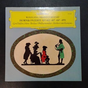 May include: Vintage vinyl record album cover featuring a light blue background with a yellow banner at the top. The album title is "HORNKONZERTE" by Wolfgang Amadeus Mozart. An oval illustration depicts silhouettes of musicians.