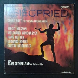 May include: Vintage vinyl record album cover for "Siegfried" featuring Georg Solti and The Vienna Philharmonic. The cover has a dark background with a silhouette of a figure holding a sword. The album title and cast are listed in white and red text.