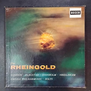 May include: A square record box set cover for Das Rheingold by the Vienna Philharmonic conducted by Solti. The cover features a glowing golden gemstone against a dark green and brown background, with the Decca logo in the top right corner.