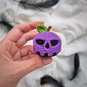 May include: A purple crocheted apple with a black skull face and a green leaf stem.