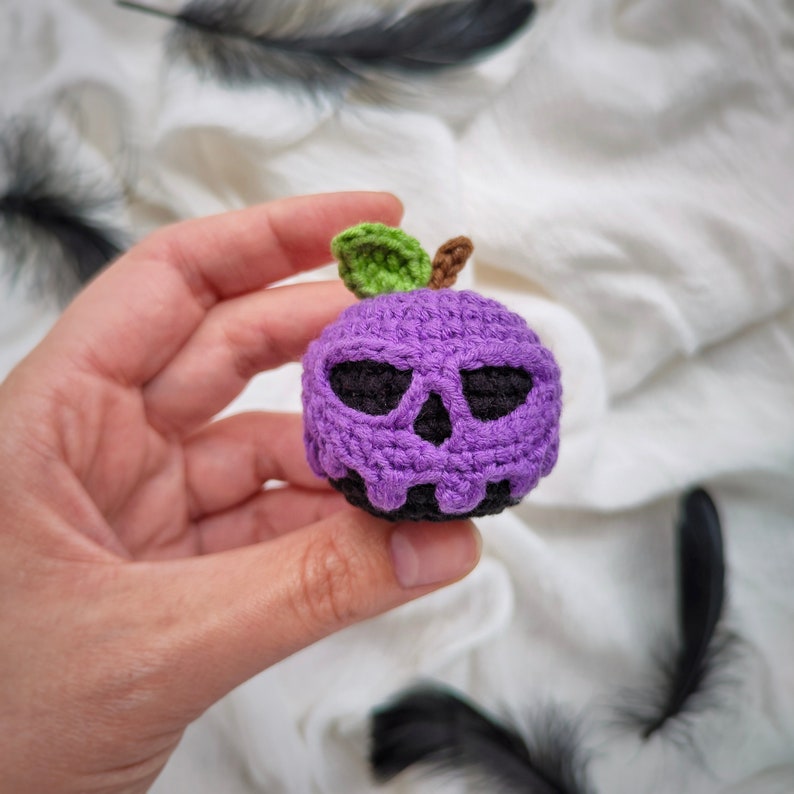 May include: A purple crocheted apple with a black skull face and a green leaf stem.
