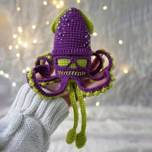 May include: Purple and green crocheted squid amigurumi toy with a skull design on the head. The squid has long tentacles and is decorated with small beads.
