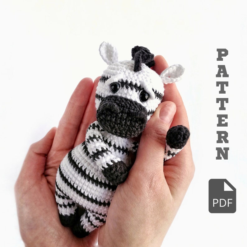 May include: A crocheted zebra toy with black and white stripes. The zebra is being held in a person's hands. The text "PATTERN PDF" is in the upper right corner of the image.