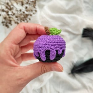 May include: A purple crocheted apple with a green leaf and black dripping icing.