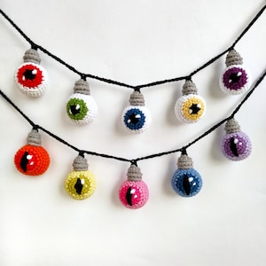 May include: A string of crocheted light bulbs with colorful eyes. Each bulb is a different color, including red, orange, yellow, green, blue, purple, and pink.