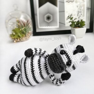 May include: A crocheted zebra toy with black and white stripes. The zebra is lying on its side with its head turned to the side. The toy has a black nose and black eyes.