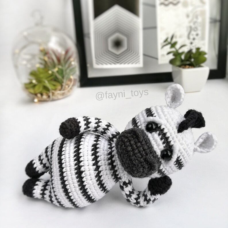 May include: A crocheted zebra toy with black and white stripes. The zebra is lying on its side with its head turned to the side. The toy has a black nose and black eyes.