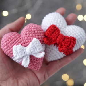 May include: Two crocheted hearts, one pink with a white bow and one white with a red bow.