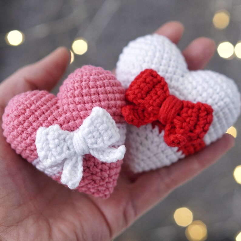 May include: Two crocheted hearts, one pink with a white bow and one white with a red bow.