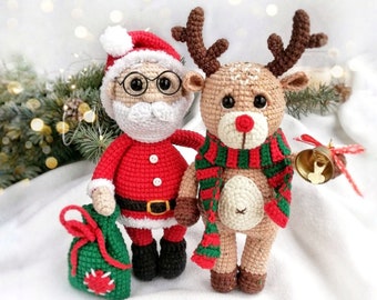 May include: A crocheted Santa Claus doll wearing a red and white suit, holding a green gift bag.  A crocheted reindeer doll with brown antlers, a red and green scarf, and a gold bell is standing next to the Santa Claus doll.
