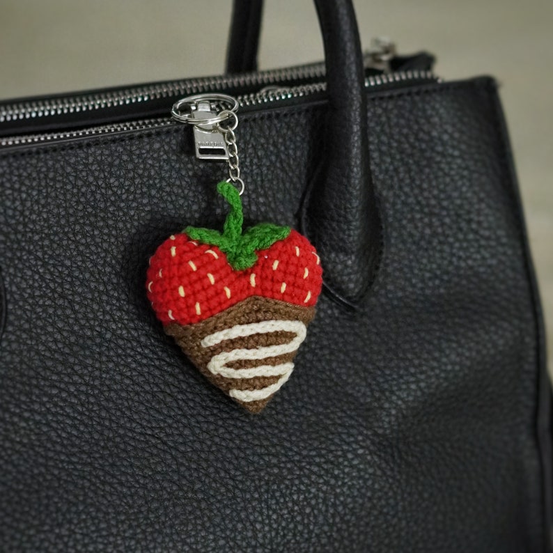 May include: A crocheted strawberry keychain with chocolate and white stripes, attached to a black leather handbag.