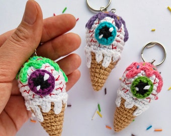 May include: Three crocheted ice cream cone keychains with googly eyes. The ice cream cones are white with colorful sprinkles and dripping white frosting. The googly eyes are purple, green, and blue.