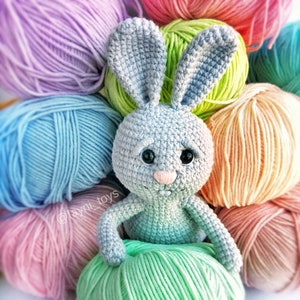 May include: A crocheted gray bunny rabbit toy surrounded by colorful yarn balls in shades of pink, blue, green, and peach.