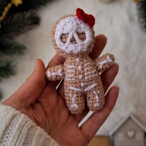 May include: A crocheted gingerbread skeleton doll with a white skull face and a small red bow. The doll's body is tan with white stitching to represent the skeleton. A unique handmade holiday decoration.