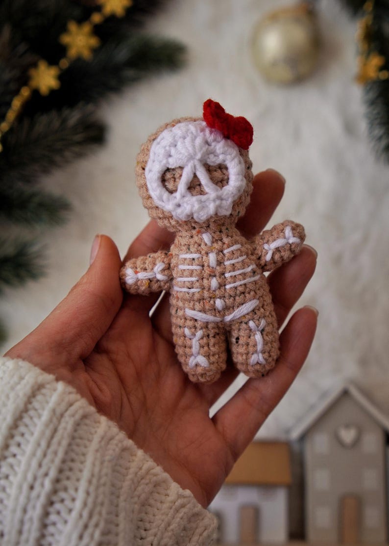 May include: A crocheted gingerbread skeleton doll with a white skull face and a small red bow. The doll's body is tan with white stitching to represent the skeleton. A unique handmade holiday decoration.