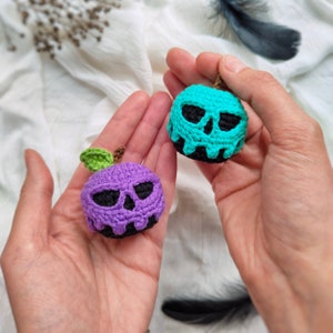 May include: Two crocheted apple ornaments with skull faces. One apple is purple and the other is teal.