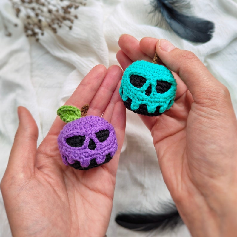 May include: Two crocheted apple ornaments with skull faces. One apple is purple and the other is teal.