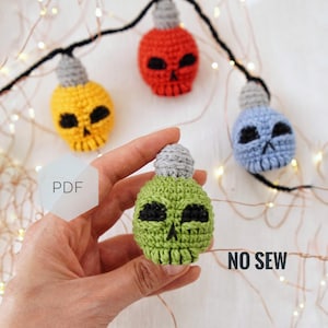 Puede incluir: Un conjunto de cuatro bombillas de ganchillo con forma de calavera en verde, amarillo, rojo y azul, cada una con una base gris y cuencas oculares negras. El texto PDF y NO SEW es visible en la imagen. Estos objetos están unidos por un hilo negro.