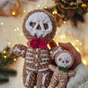 May include: Two crocheted skeleton dolls. The larger doll is brown with white bone detailing, a white skull face, and a pink bow tie. The smaller doll is tan with white bone detailing, a white skull face, and a green bow tie.