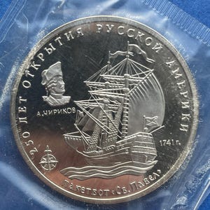 May include: A silver coin celebrating the 250th anniversary of the discovery of Russian America. The coin shows a sailing ship, a portrait, and Cyrillic text. The year 1741 is also visible.