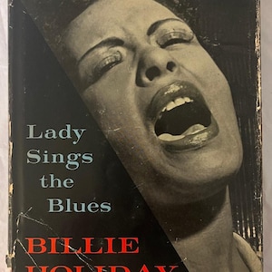 May include: Vintage book cover for "Lady Sings the Blues" by Billie Holiday. The cover features a black and white image of Billie Holiday singing, with her mouth open. The title and author's name are in white and red text.