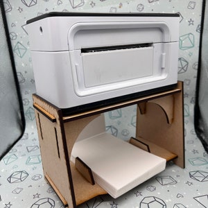 May include: A white photo printer sits on a wooden stand with a stack of white paper. The printer has a black top and a slot for inserting paper.