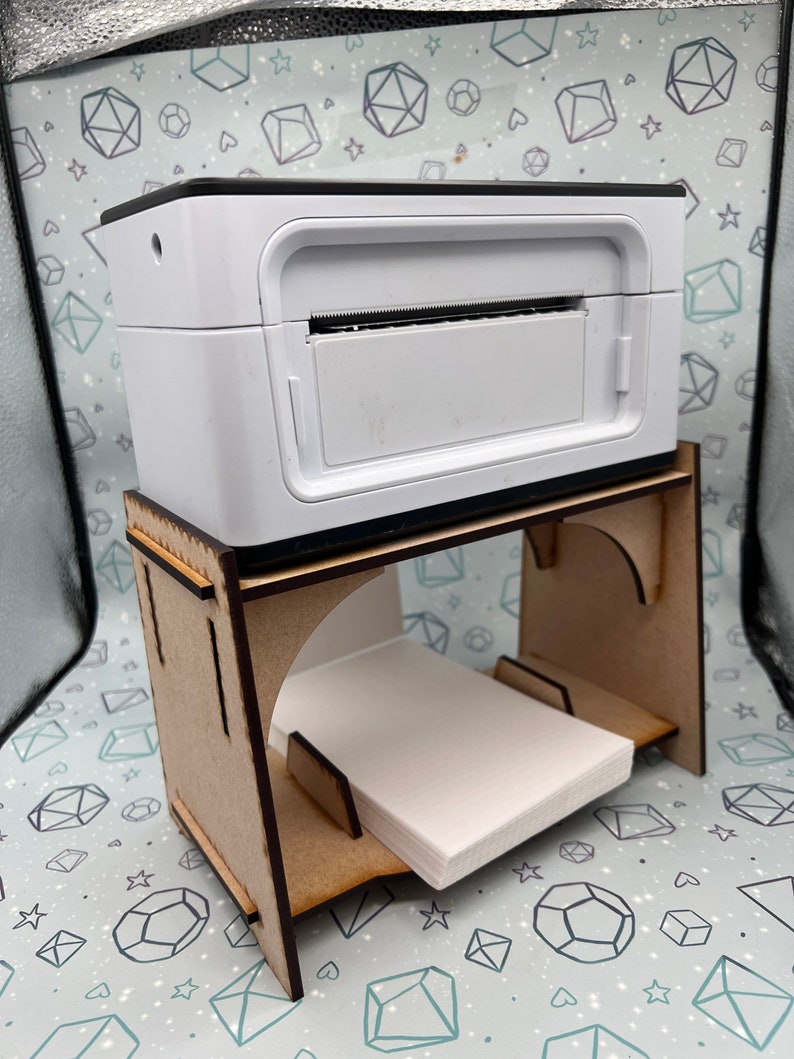 May include: A white photo printer sits on a wooden stand with a stack of white paper. The printer has a black top and a slot for inserting paper.