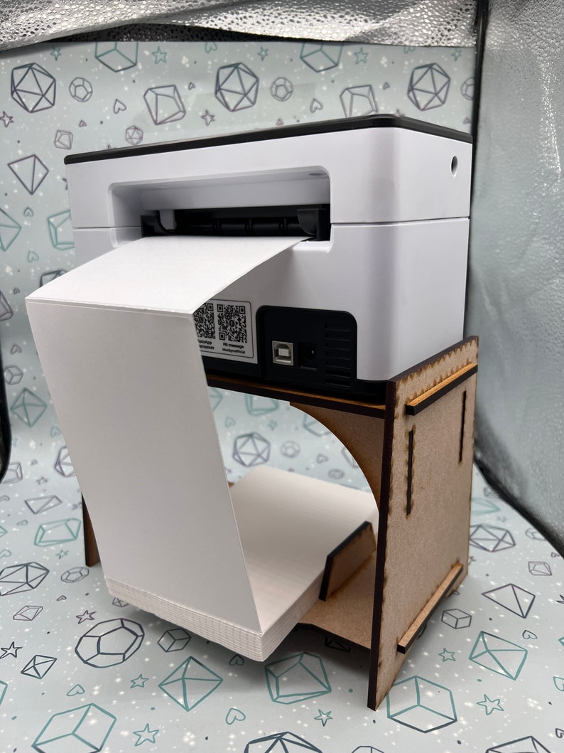 May include: A white label printer with a roll of paper feeding through it. The printer is sitting on a wooden stand.